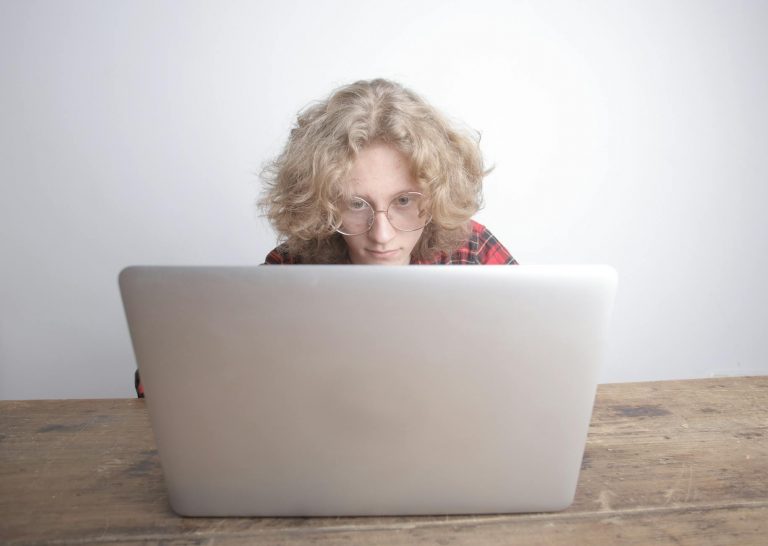 Professional person working on laptop at home office in evening, warm lighting, documents and coffee on desk, modern apartment setting, focused and determined expression, side hustle concept, realistic photography style, cozy productive atmosphere — Formations 90
