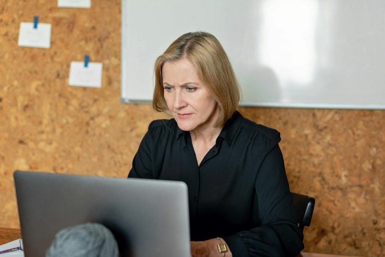 Professional woman or man in their 40s looking at computer screen showing training programs and digital learning interface, modern office environment, bright natural lighting, focused expression showing determination and career growth, laptop and documents on desk, keywords: professional training, career change, digital learning, adult education — Formations 90